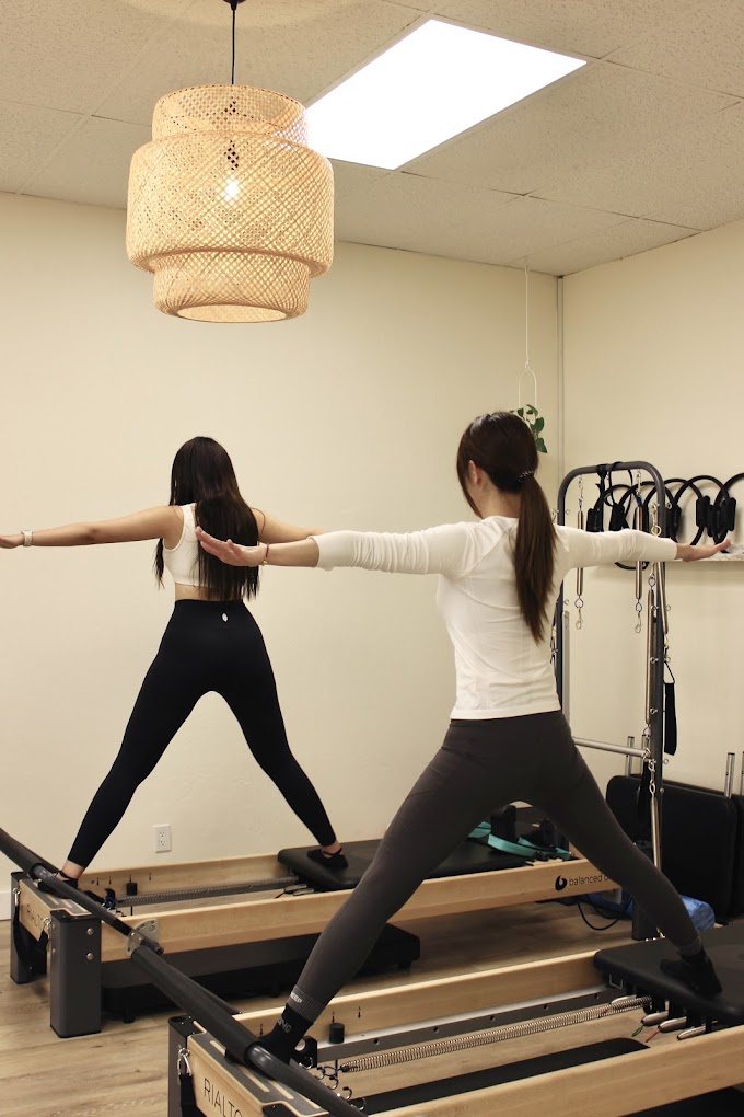 Two clients standing on the reformers with arms extended during a balance sequence